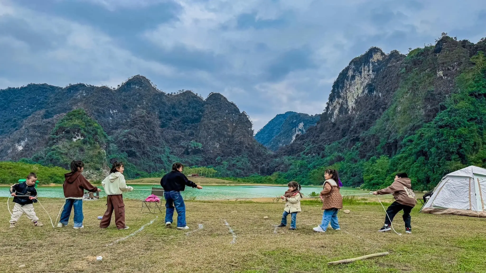 Khách vui chơi trên bãi cỏ trước dãy núi đá